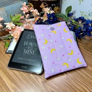 Puede incluir: Un lector de libros electrónicos Kindle con una funda protectora. La funda es de color lila claro y presenta un estampado de lunas crecientes amarillas, conejitos blancos y estrellas rosas. El Kindle muestra el título del libro "ON YOUR MINE" de Morgan Bridges.