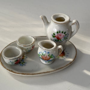 May include: A miniature porcelain tea set with floral designs. The set includes a teapot, creamer, two cups, and a tray.