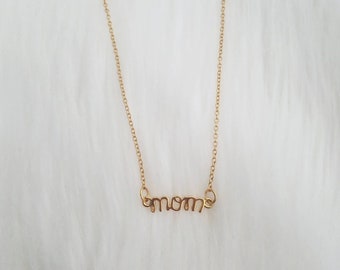 Puede incluir: Un collar de oro con un colgante de 'mamá' en letra cursiva.