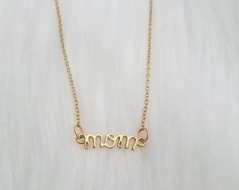 Puede incluir: Un collar de oro con un colgante de 'mamá' en letra cursiva.