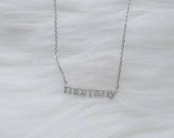 Puede incluir: Un collar de plata con una cadena delicada y un colgante que dice "mamá".