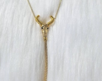 May include: A gold chain necklace with a bull's head pendant. The pendant has black eyes and a detailed design.