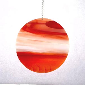 Pode incluir: Um apanhador de sol redondo em vitral com uma vibrante combinação de vermelho e laranja. O vidro apresenta um design em camadas com riscas brancas e um pequeno detalhe vermelho mais escuro. Uma corrente prateada está presa para pendurar.