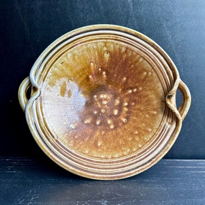 May include: A brown ceramic serving dish with two handles. The dish has a speckled glaze and a raised rim.
