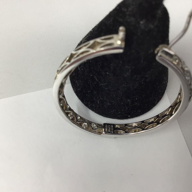 May include: Silver hoop earrings with a delicate, intricate design and small clear stones set around the edge.