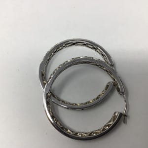 May include: A pair of silver hoop earrings with a detailed design. The earrings are made of metal and have a polished finish.