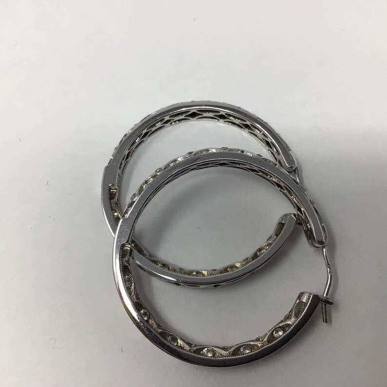 May include: A pair of silver hoop earrings with a detailed design. The earrings are made of metal and have a polished finish.