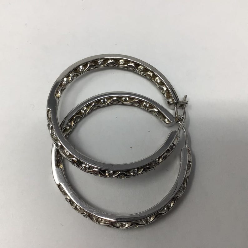 May include: A pair of silver hoop earrings with a decorative design of small round stones around the edge.