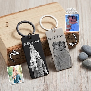 May include: Two rectangular keychains with engraved photos and text. One black keychain says "Daddy & Noah" and the other silver keychain says "Best Dad Ever." Both have a metal ring for keys. A small photo is shown next to each keychain.