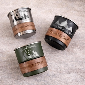 K&ouml;nnte beinhalten: Drei Reisebecher mit eingravierten Designs. Einer ist silberfarben, einer schwarz und einer olivgr&uuml;n. Jeder Becher hat ein Holzband mit personalisiertem Text. Der silberne Becher tr&auml;gt die Aufschrift "Travel Together" und "HENRY & FATHER". Der schwarze Becher tr&auml;gt die Aufschrift "Breath deep, be here" und "David & Dad". Der olivgr&uuml;ne Becher tr&auml;gt die Aufschrift "Travel Together" und "ANDREW & PAPA".