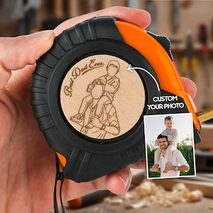 May include: Black and orange tape measure with a wooden insert featuring a custom photo and the words "Best Dad Ever." The tape measure is held in a hand, with the measuring tape extended.