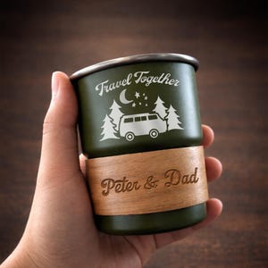 K&ouml;nnte beinhalten: Gr&uuml;ner Reisebecher mit silbernem Rand und Holzsockel. Der Becher tr&auml;gt den Text "Travel Together" mit einer Grafik von Van, B&auml;umen, Mond und Sternen. Der Sockel ist mit "Peter & Dad" graviert.