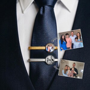 May include: A gold tie clip with the text "BEST DAD EVER" and a photo of a family. A silver tie clip with the text "WORLD'S GREATEST PAPA" and a photo of a family. The tie clips are on a navy blue tie.