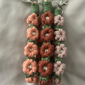 May include: Three crocheted keychains with flower designs. The keychains are in shades of pink, orange, and green.