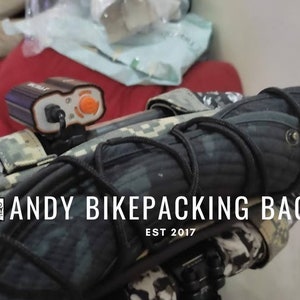 Könnte beinhalten: Eine schwarze und graue Bikepacking-Tasche mit Tarnmuster und dem Text "ANDY BIKEPACKING BAGS EST 2017".