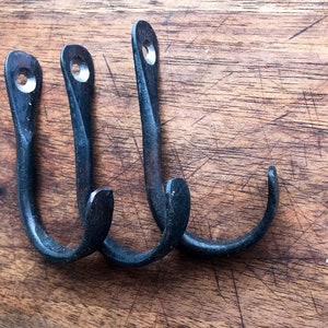 Könnte beinhalten: Drei schwarze Metallhaken mit gehämmerter Oberfläche. Die Haken sind auf einer Holzoberfläche montiert.