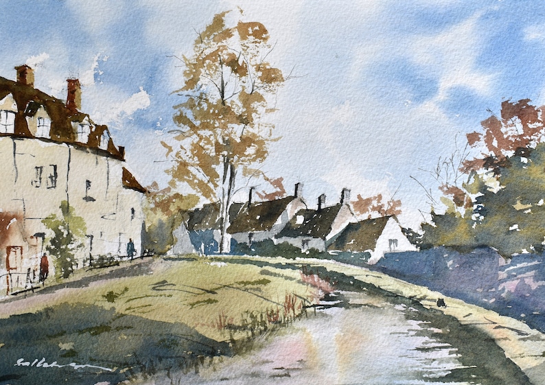 May include: Watercolor painting of a quaint village scene. White buildings with brown roofs line a grassy bank, with a tree in the center. A waterway flows in the foreground under a blue sky with clouds. The artwork is signed in the lower left corner.