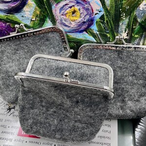 May include: Three grey felt coin purses with silver metal frames and clasps. The purses are stacked on top of each other.