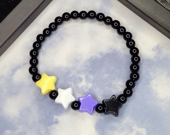 May include: A black beaded bracelet with yellow, white, and purple star charms. The bracelet is on a white and blue background.