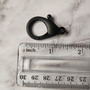 May include: Black plastic swivel clasp with a spring-loaded gate. The clasp is approximately 2.5 cm in length.
