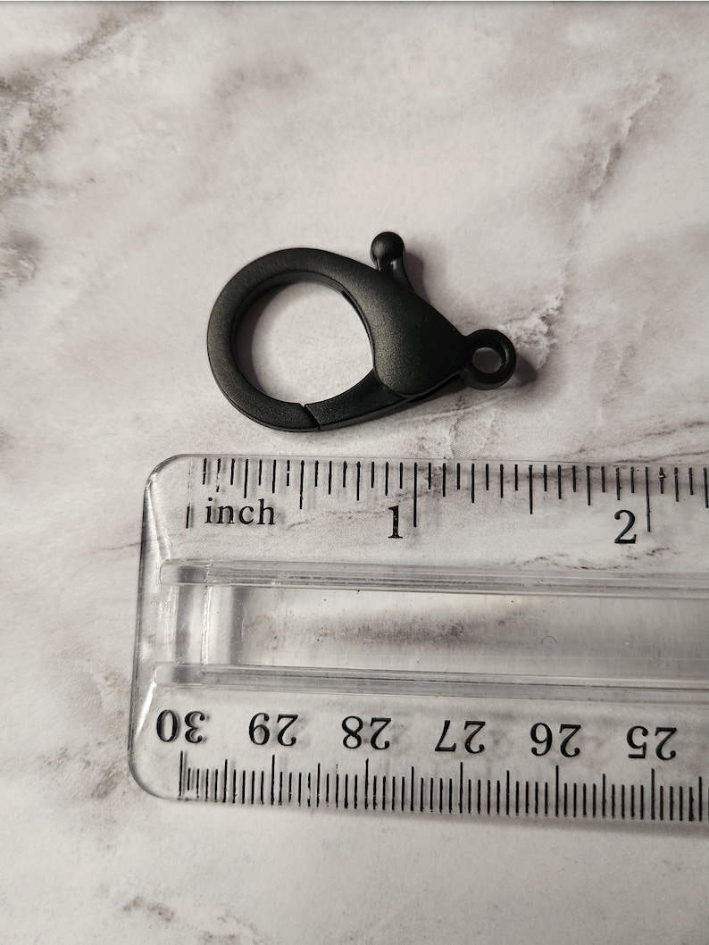 May include: Black plastic swivel clasp with a spring-loaded gate. The clasp is approximately 2.5 cm in length.