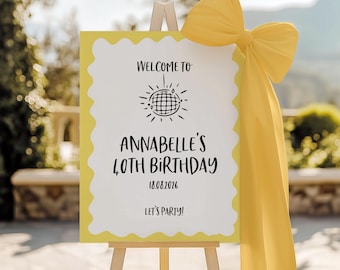 May include: A yellow and white welcome sign on an easel, with the text "Welcome to Annabelle's 40th Birthday" and the date 18.08.2026. A large yellow bow adorns the top right corner. The sign is designed for a party.
