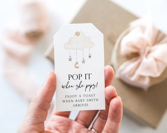 Può includere: Un biglietto bianco con un design di nuvola e stelle. Il testo sul biglietto recita "POP IT when she pops! ENJOY A TOAST WHEN BABY SMITH ARRIVES".