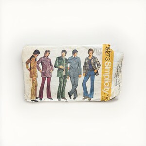 May include: A vintage Simplicity sewing pattern envelope, number 8273, featuring illustrations of five outfits including jackets, trousers, and shirts. The white paper envelope has a yellow vertical strip on the right side with black text.