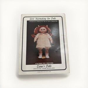 May include: A book titled "Yarn Hairmaking For Dolls" with a doll image on the cover. The doll has red yarn hair and wears a white dress. The book also includes the text "4 PATTERNS FOR 4 HEAD SIZES" and "Teena's Dolls".
