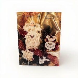 May include: A Christmas-themed display featuring two angel figurines with white lace dresses and red accents. The display includes a gold background, red ribbon with gold stars, and the text "CROSS PATCH".