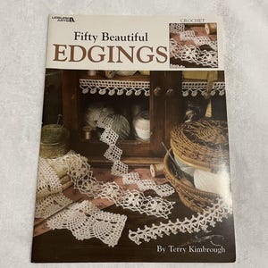 May include: A softcover instructional book titled Fifty Beautiful EDGINGS by Terry Kimbrough. The cover features a photograph of various white crocheted lace trims displayed on a wooden surface with a woven basket and spools of thread.