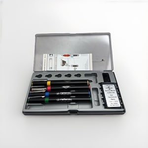 May include: A black pen set in a gray plastic case. The set includes several black pens with colored bands, a small bottle of India ink, and an instruction sheet. The pens are labeled "reform" and "ALVIN".