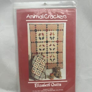 May include: A sewing pattern packet titled Animal Crackers by Elizabeth Quilts, enclosed in a clear plastic sleeve. The cover features a photograph of a large quilt and a smaller matching quilt, both decorated with various animal silhouettes.