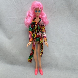 May include: A vintage doll with pink curly hair and blue eyes. The doll wears a colorful patterned coat with orange, green, and yellow circles. She is also wearing pink shoes.