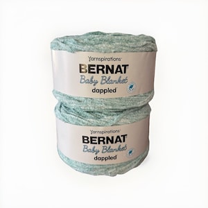 May include: Two stacked rolls of Bernat Baby Blanket dappled yarn. The yarn is a soft, plush material in a light teal color. Each roll has a white label with the brand name and product information.
