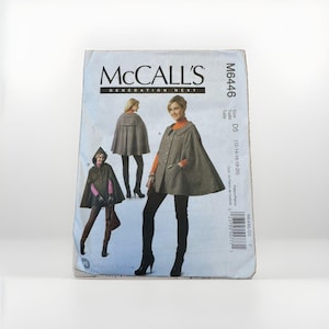 May include: A McCall's M6446 sewing pattern envelope for a cape. The front displays two variations of a grey cape, one with a hood and one with a collar, worn over dark clothing. The text includes the brand name, pattern number, and size range D5.