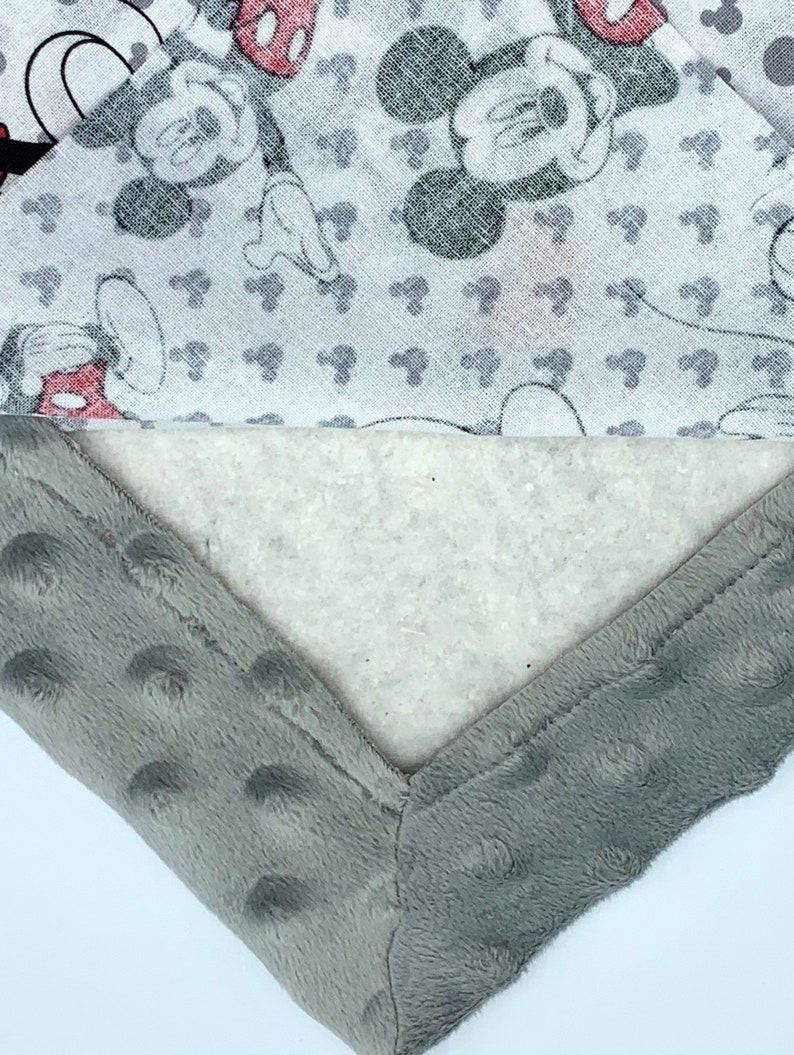 May include: A gray and white baby blanket with a Mickey Mouse print. The blanket has a soft, plush texture and is perfect for cuddling.