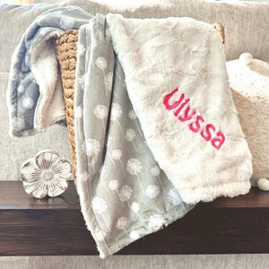 May include: A gray and white patterned blanket with a white fluffy blanket on top. The fluffy blanket has the name "Alyssa" embroidered on it in pink.