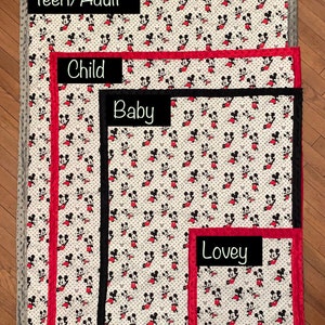 May include: Size reference for Mickey Mouse blankets in four sizes: Teen/Adult, Child, Baby, and Lovey. The blankets are white with a red and black Mickey Mouse print. The Teen/Adult blanket has a gray border, the Child blanket has a red border, the Baby blanket has a black border, and the Lovey blanket has a red border.