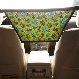 May include: A child in a car seat with pink socks and blue jeans. A green and black fabric sunshade with a jungle animal print is hanging from the headrest.