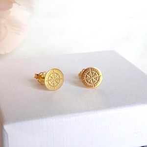 May include: A pair of gold compass earrings. The earrings are small and round, with a compass design in the centre.