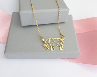 May include: A gold necklace with a geometric elephant pendant. The necklace is displayed on a gray box with a pink ribbon.