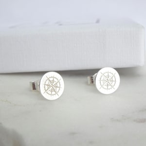 May include: A pair of silver stud earrings with a compass design. The compass is engraved on a round disc.