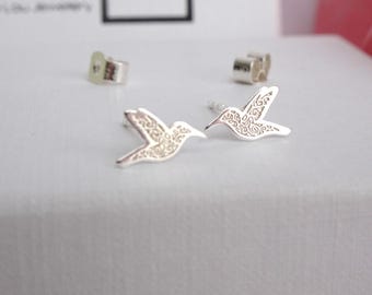 May include: A pair of silver stud earrings shaped like hummingbirds, featuring intricate engraved scrollwork patterns on the surface. The earrings include matching silver butterfly-style earring backs positioned behind the main hummingbird studs.
