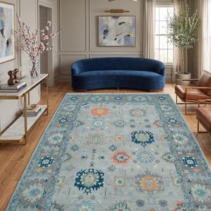May include: A rectangular area rug featuring a light gray base with a repeating pattern of floral and geometric motifs in shades of orange, dark blue, light blue, and sage green, framed by a wide border with matching decorative elements.