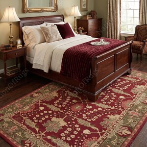 May include: A rectangular area rug featuring a deep red background with intricate floral and vine patterns in shades of sage green, cream, and muted pink. The rug has a wide border with repeating botanical motifs and sits on a dark wood floor.