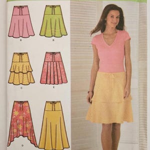 May include: Simplicity easy-to-sew pattern featuring skirt designs. The pattern includes various skirt styles in pink, green, yellow, and floral prints. The model is wearing a pink top and a yellow skirt with a dotted pattern. Size UU 16,18,20,22.