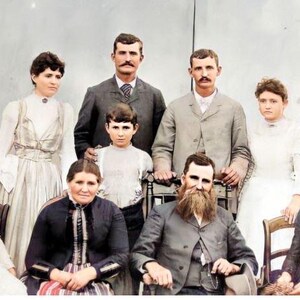 May include: A vintage photograph of a family portrait. The family are dressed in formal attire, with the men wearing suits and the women wearing dresses. The family are posed in a traditional portrait style, with the parents standing at the back and the children sitting at the front. The photograph is in colour and has a warm, nostalgic feel.