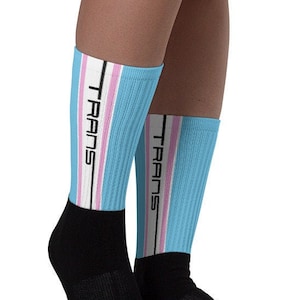 Puede incluir: Un par de calcetines azules con rayas blancas y rosas y la palabra "TRANS" impresa en cada calcetín.