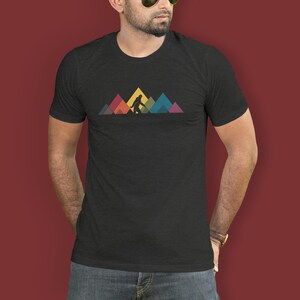 May include: A black t-shirt featuring a graphic of Bigfoot walking across a mountain range. The mountains are made up of colourful geometric shapes.